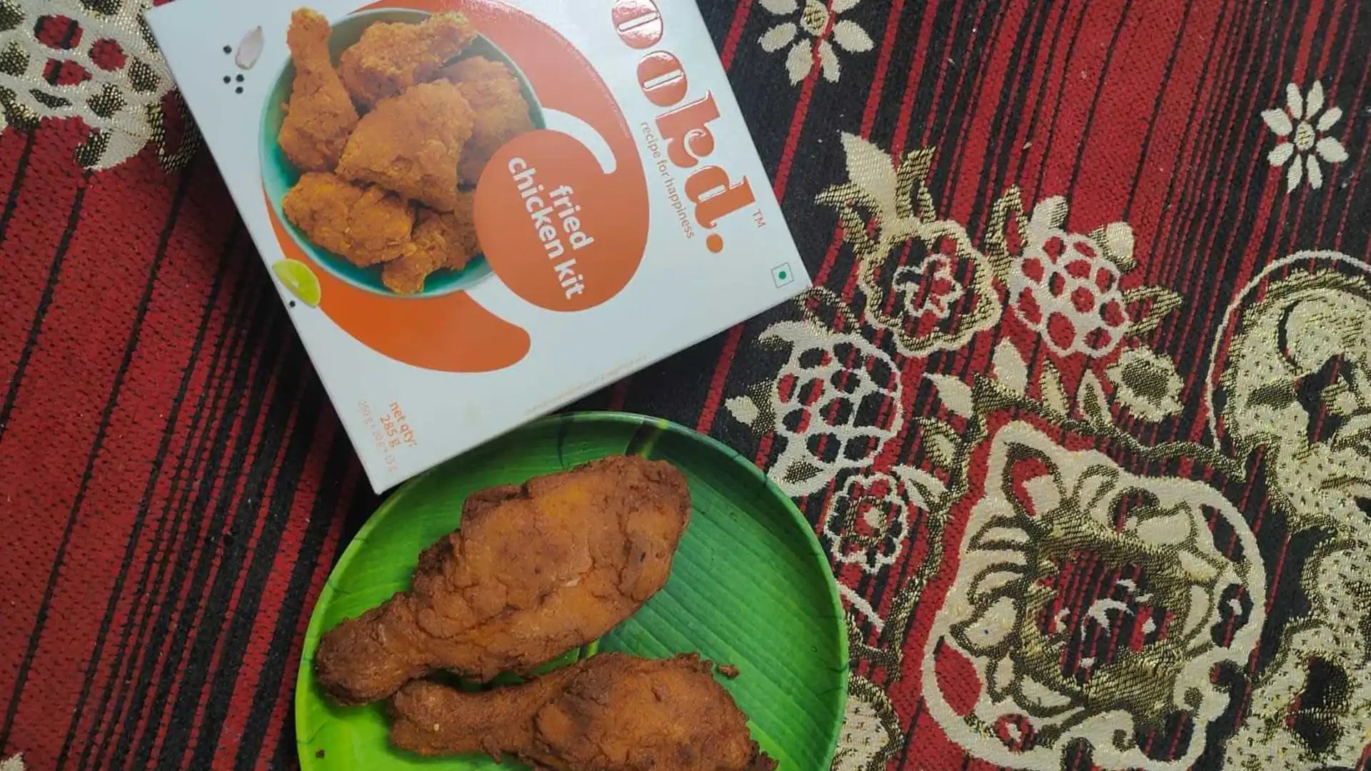 Fried chicken on a green plate with a Pokidz branded box on a decorative fabric background