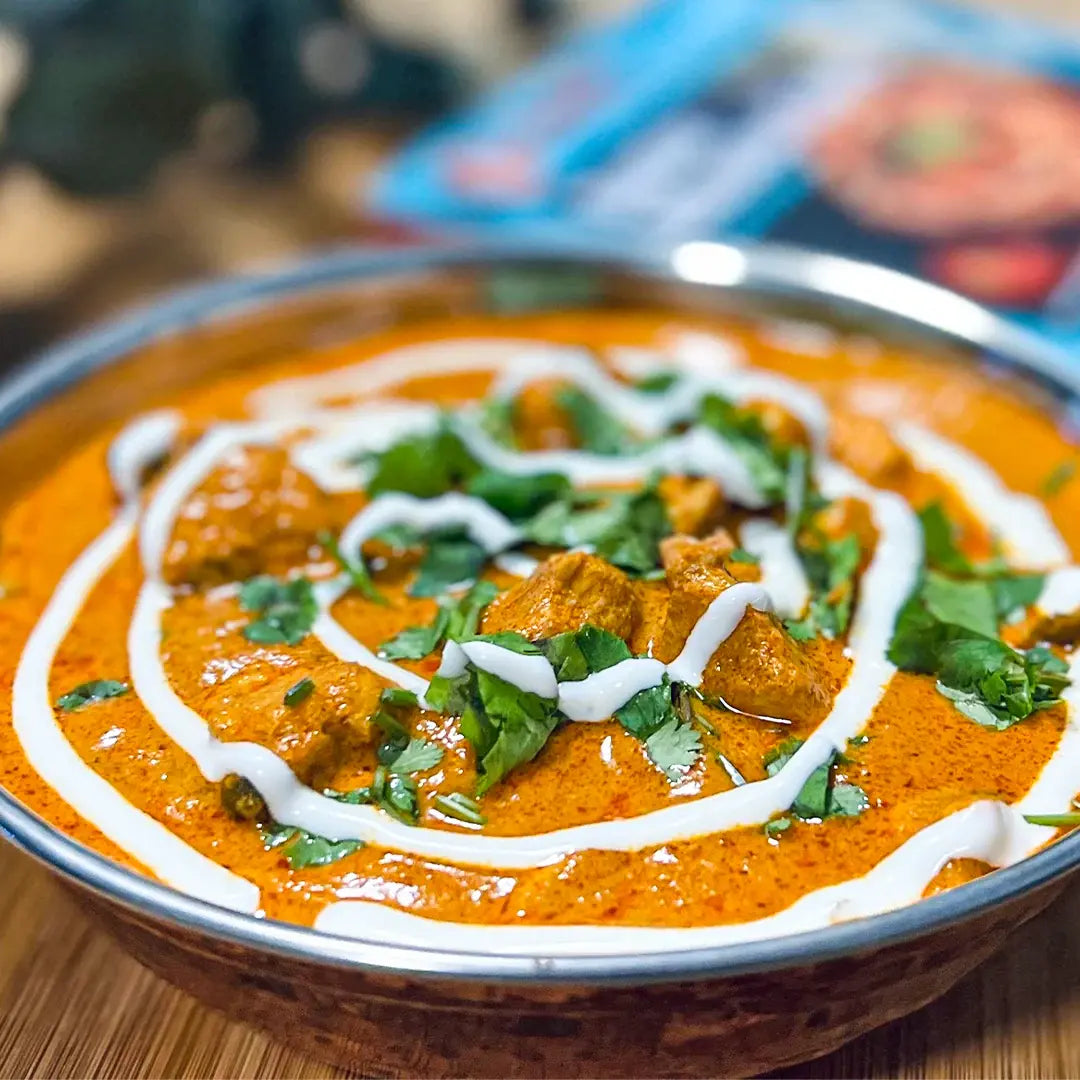 Bowl of orange curry with white sauce and green herbs on a wooden table.